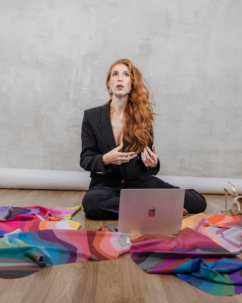 Bárbara Salgueiro sentada no chão do atelier, rodeada de tecidos de cor, durante uma sessão de diagnóstico.