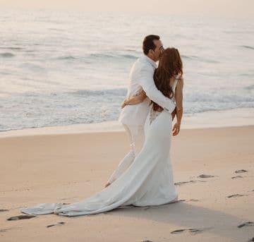 Bárbara Salgueiro e o marido abraçados na praia, em vestido de noiva.